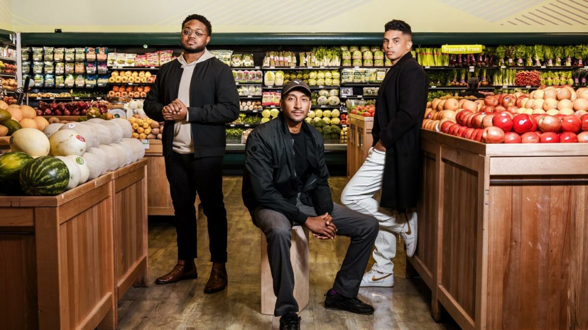 three men pose in a grocery store