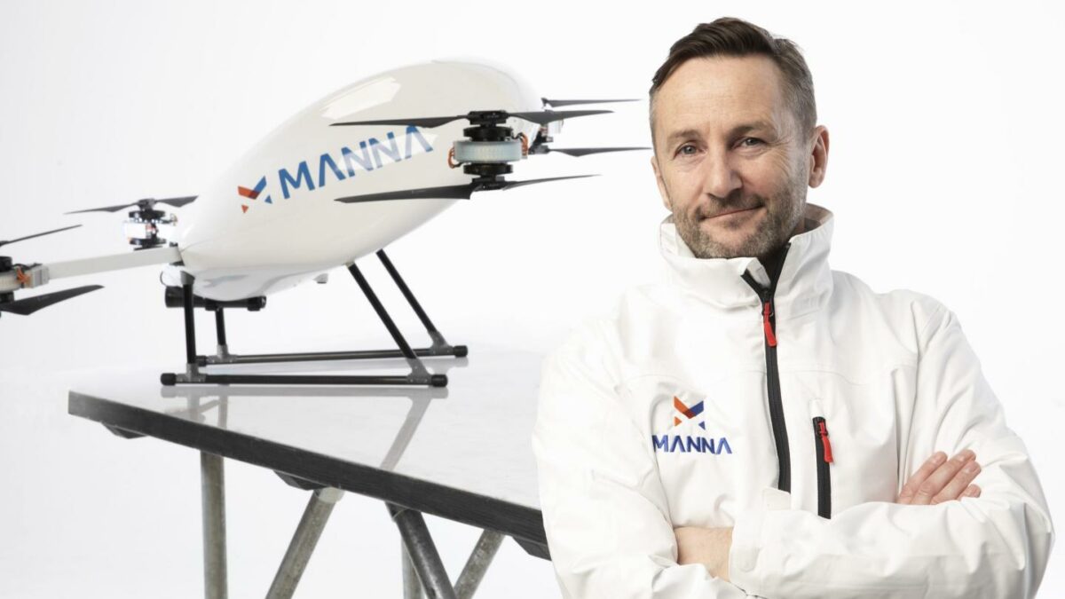 Bobby Healy stands in front of a Manna drone with his arms crossed.
