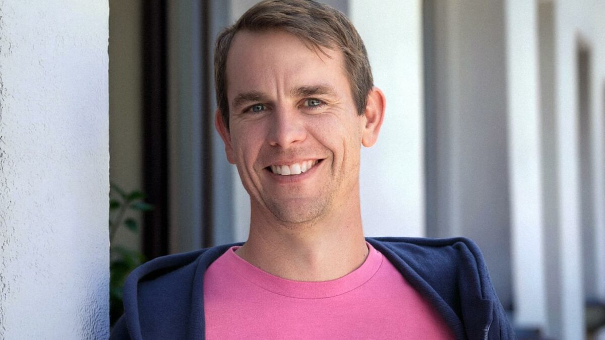 Colin Zima smiles while wearing a pink shirt