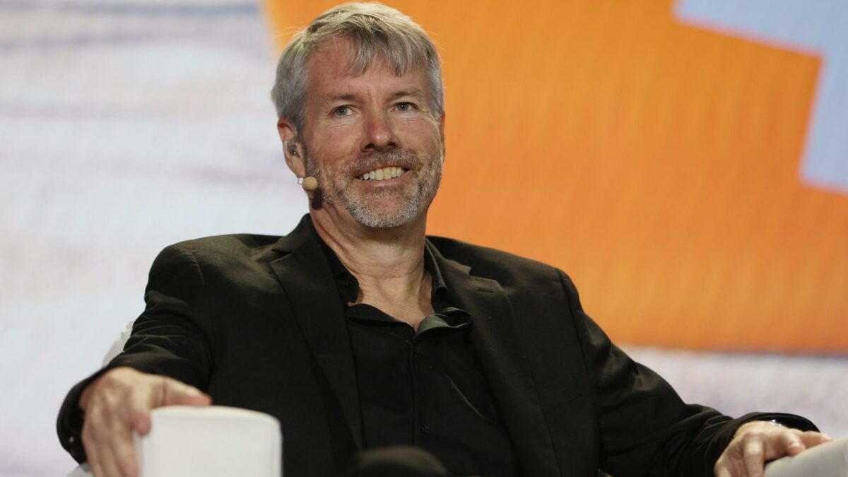 Michael Saylor sitting during a conference and smiling while looking into the distance.