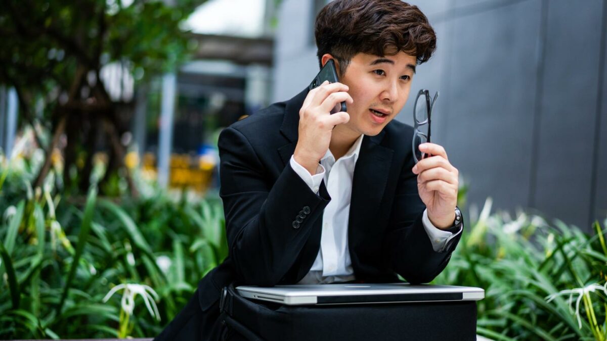 Asian man talking on the phone with his laptop in his lap