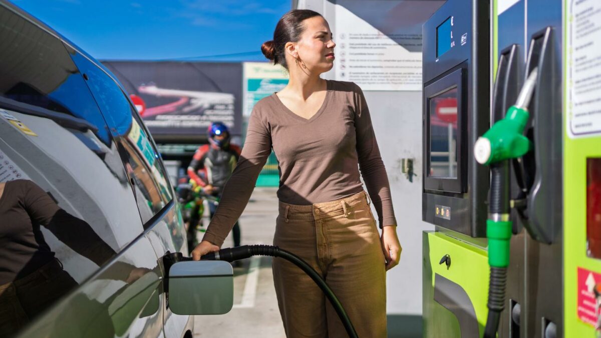 Woman refuels her car at a gas station on a sunny day, pondering rising gas prices and environmental impact. Transportation, energy, and the environment intersect in daily life