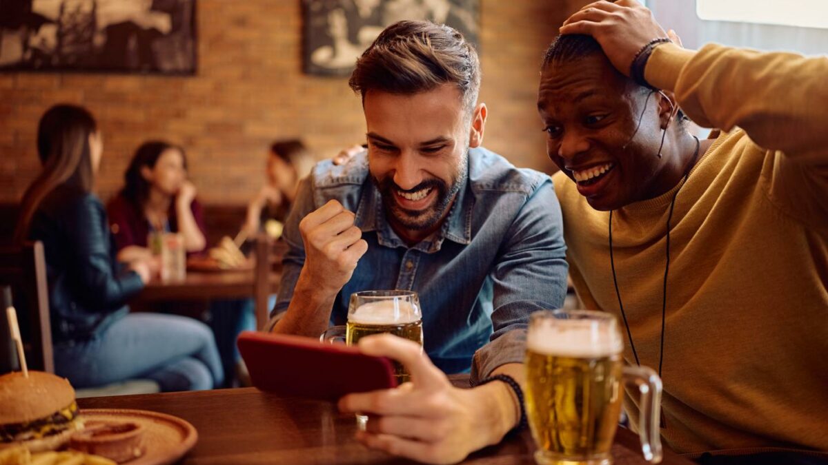 Two men in a sports bar are happy as they look at a phone