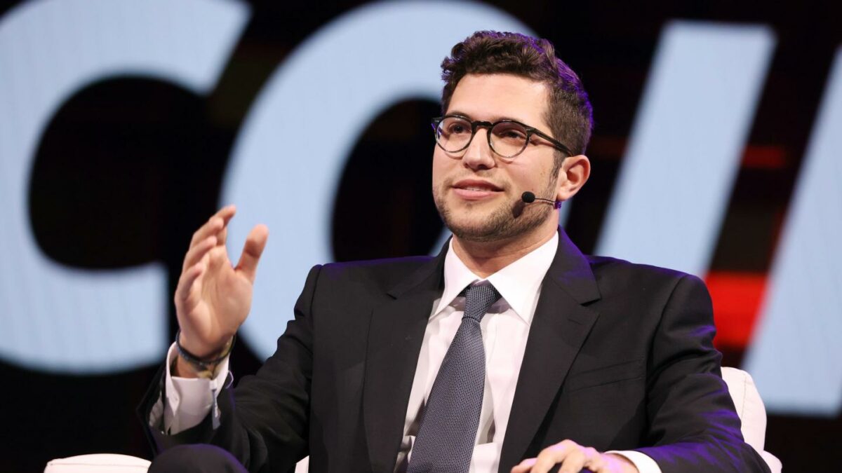 Brandon Lutnick, chairman of Cantor Fitzgerald, sits in a white chair wearing a suit and speaking.