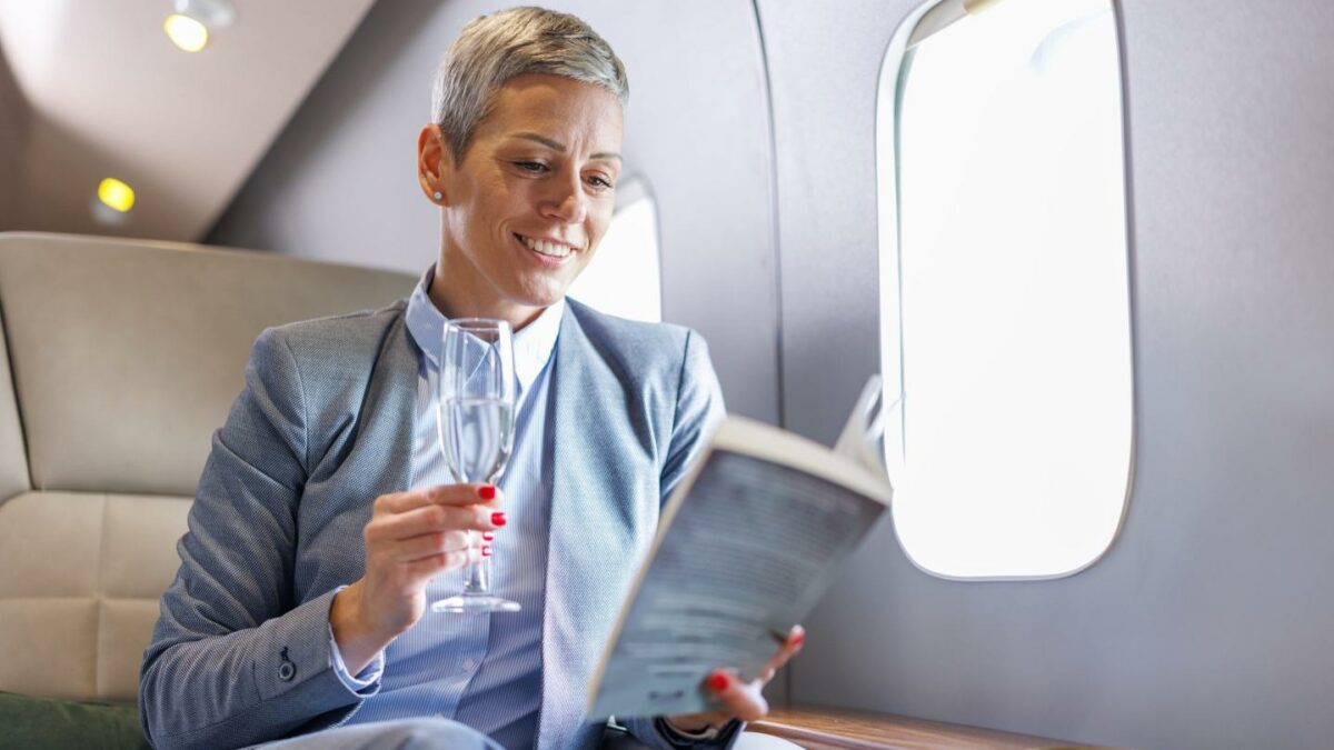 Businesswoman reading a book on private jet while drinking champagne