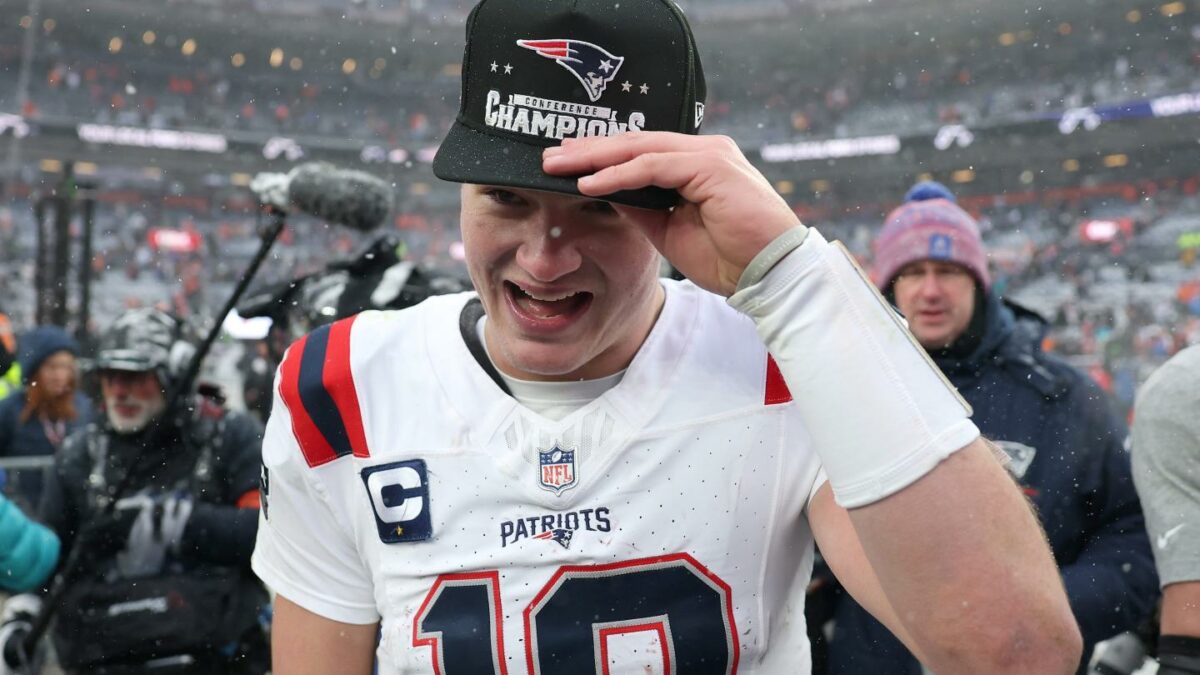 Drake Maye holds onto an AFC Conference Champion hat as he smiles on the field.