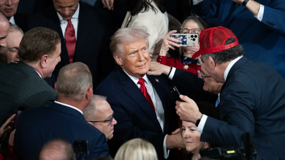 A man wearing a red hat shakes Trump's hand in a crows